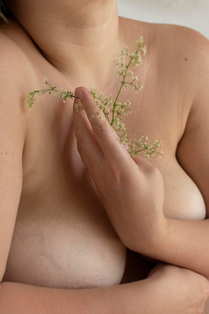 Femme posant avec confiance dans le nu et tenant une fleur entre ses seins