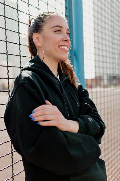 Femme positive avec une coiffure sombre portant une tenue sombre souriant et s'amusant dans la ville en journée chaude et ensoleillée