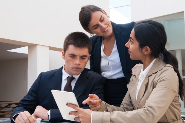 Femme positive montrant l&#39;écran de la tablette aux hommes d&#39;affaires