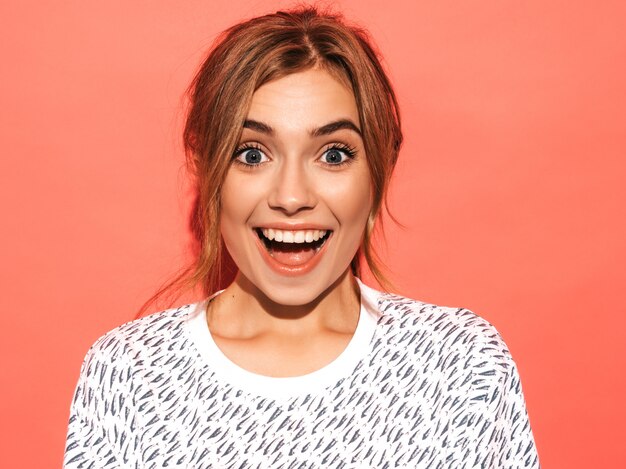 Femme positive souriant. Modèle drôle posant près d'un mur rose en studio. Choqué et surpris