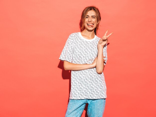 Femme positive souriant. Modèle drôle posant près d'un mur rose en studio.