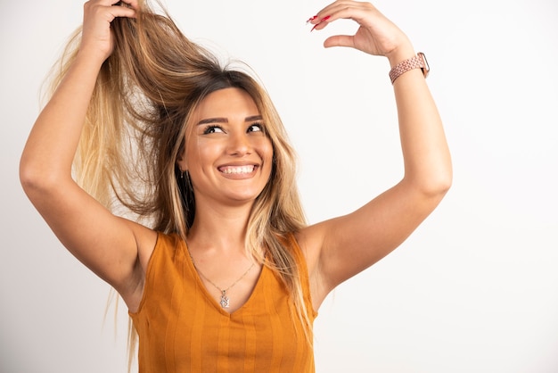 Femme positive touchant ses cheveux et posant sur fond blanc.