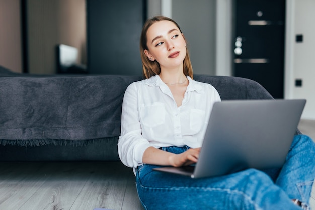 Femme positive utilisant l'ordinateur portable à la maison assise sur le sol