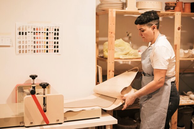 Femme potier en tablier aplatissant l&#39;argile à l&#39;intérieur du papier avec une machine