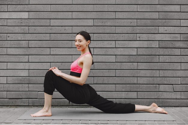 Femme pratiquant le yoga avancé contre un mur urbain sombre