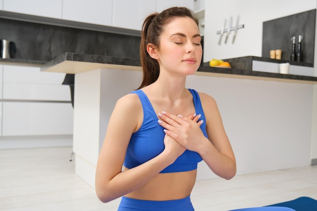 Photo gratuite femme pratiquant le yoga et la méditation à la maison assise dans la pose du lotus sur un tapis de yoga détendue avec fermé