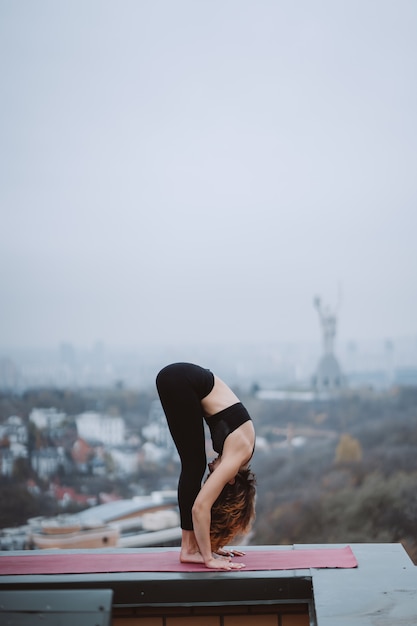 Femme pratiquant le yoga sur le tapis sur le toit et faire des exercices de yoga