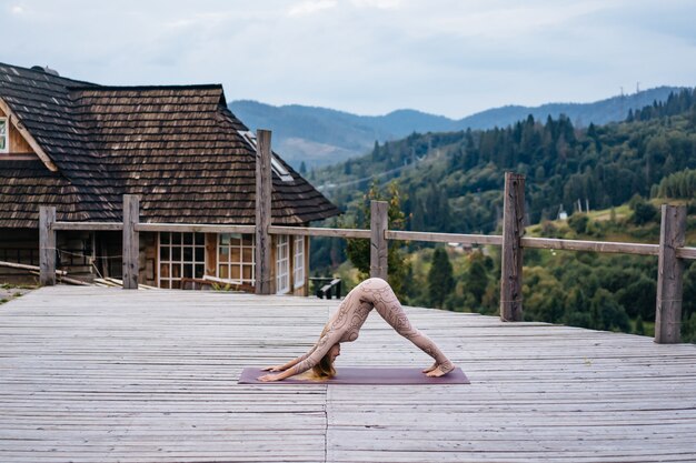 Une femme pratique le yoga le matin sur une terrasse au grand air.