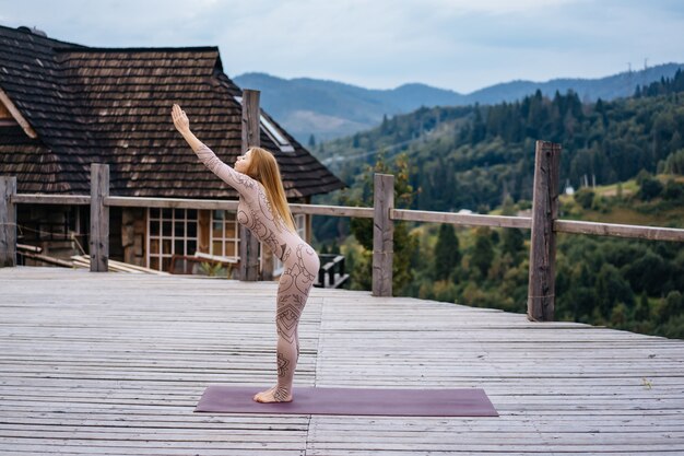 Une femme pratique le yoga le matin sur une terrasse au grand air.