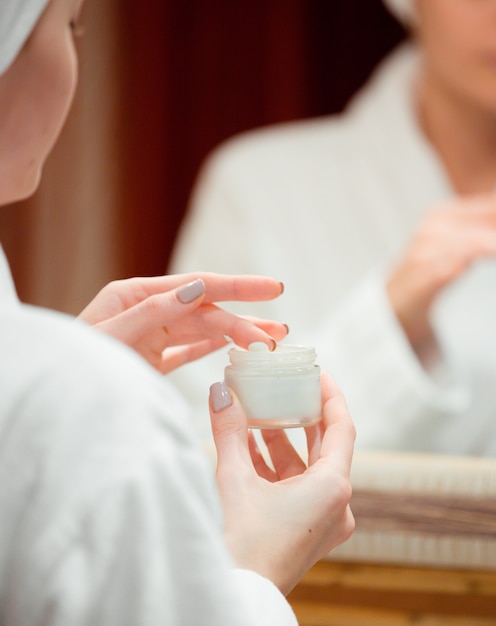 Photo gratuite femme prenant une crème pour le visage avec son doigt dans la salle de bain