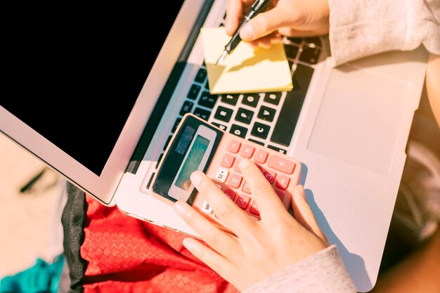 Femme prenant des notes à la main sur un ordinateur portable en journée ensoleillée