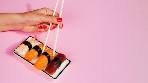 Femme prenant une paix de sushi avec des baguettes de la plaque