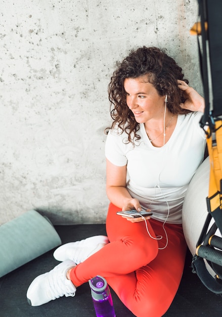 Femme prenant une pause après l&#39;entraînement et écoutant de la musique sur téléphone portable dans la salle de sport