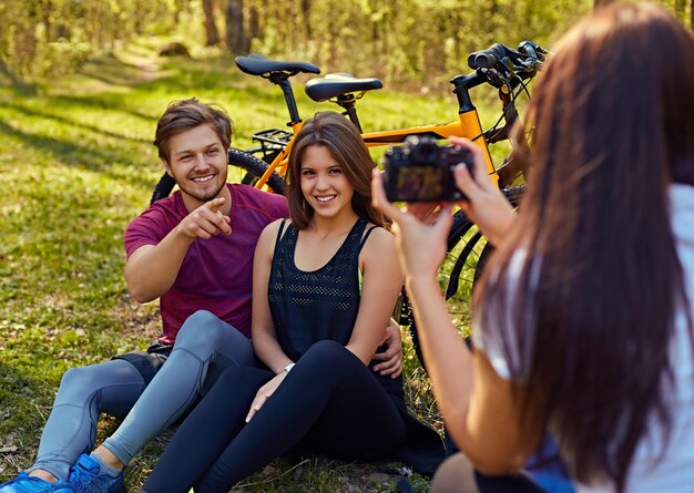 Une femme prenant des photos de couple sportif après une balade à vélo dans une forêt.