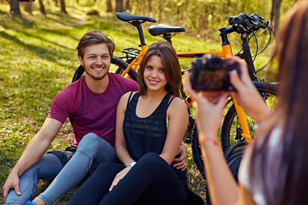 Une femme prenant des photos de couple sportif après une balade à vélo dans une forêt.