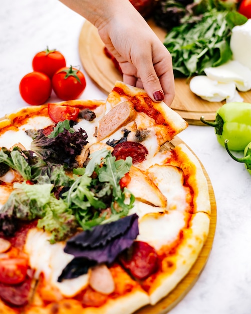 Femme prend une tranche de pizza mixte avec pepperoni, dinde à la saucisse et herbes