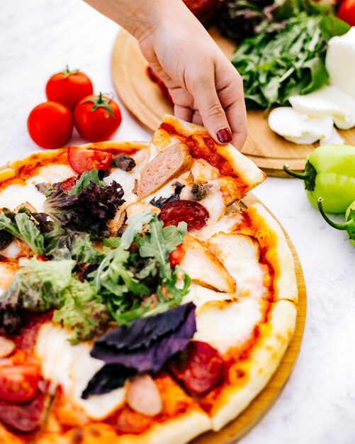 Femme prend une tranche de pizza mixte avec pepperoni, dinde à la saucisse et herbes