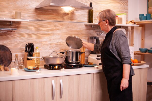 Femme préparant de la nourriture sur une cuisinière à gaz pour un dîner romantique avec son mari. Femme à la retraite cuisinant des aliments nutritifs pour elle et son homme pour célébrer l'anniversaire de la relation.