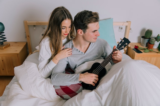 Photo gratuite femme près d'un homme qui joue du ukulélé au lit
