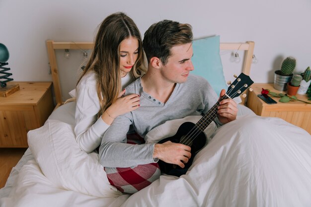 Femme près d&#39;un homme qui joue du ukulélé au lit