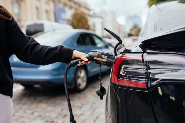 Femme près de voiture électrique. Véhicule chargé à la station de charge.