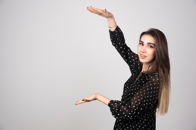 Femme présentant quelque chose sur un fond gris.