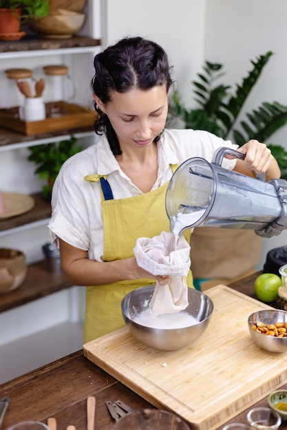 Femme pressant le lait d'amande d'amande dans la cuisine à la maison