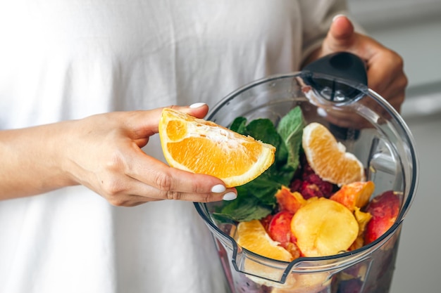 Une femme presse du jus d'orange dans un mélangeur pour faire un smoothie de fruits et des boissons d'été.