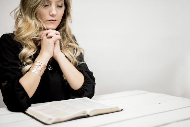 Femme priant devant la bible sur une table sous les lumières