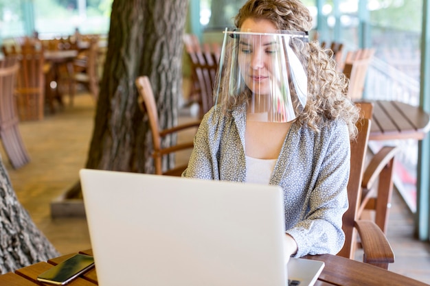 Femme avec protection du visage tout en travaillant sur un ordinateur portable