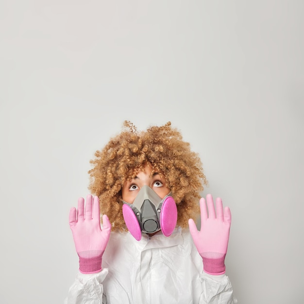 Une femme prudente garde les paumes vers la caméra pour se protéger a des problèmes écologiques n'a pas d'air frais pour respirer porte un masque à gaz et des gants de protection blancs