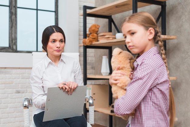 Photo gratuite femme psychologue ayant une séance de thérapie avec une fille triste tenant un ours en peluche dans la main