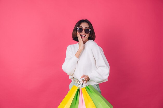 Femme en pull blanc décontracté et lunettes de soleil sur mur rouge