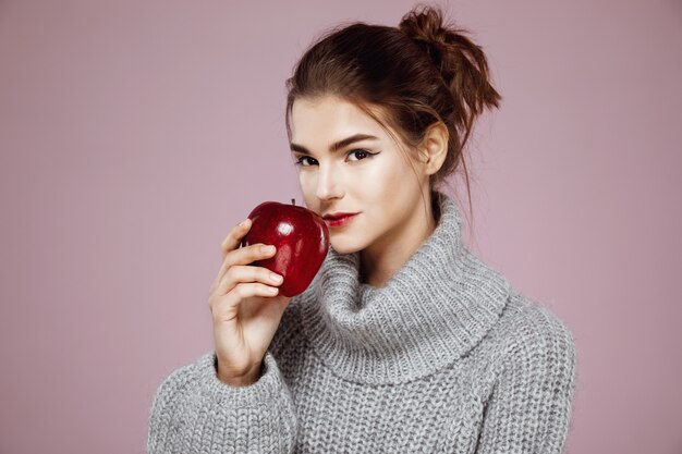 femme en pull gris souriant tenant la pomme rouge.