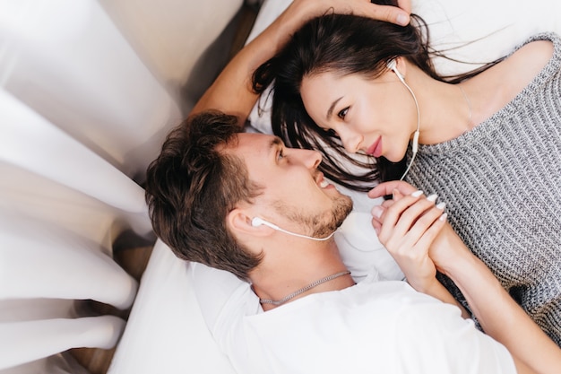 Femme en pull tricoté à l'écoute de la musique avec son petit ami pendant le repos au lit