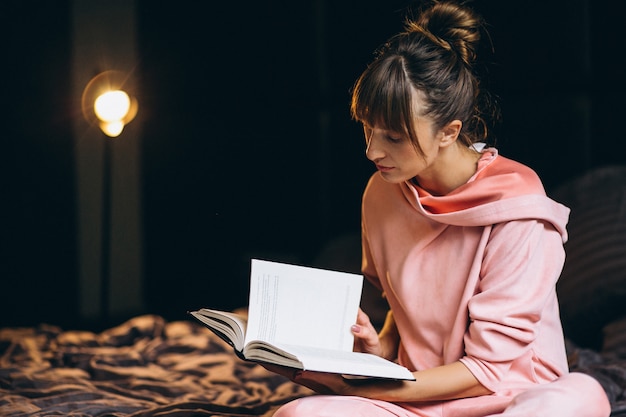 Femme en pygama assise dans son lit et livre de lecture