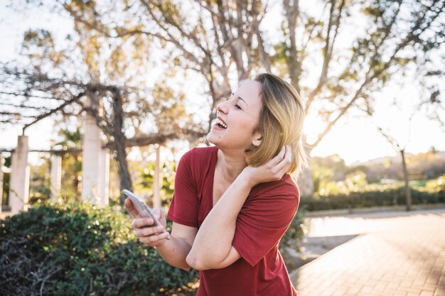 Femme qui riante avec smartphone dans le parc