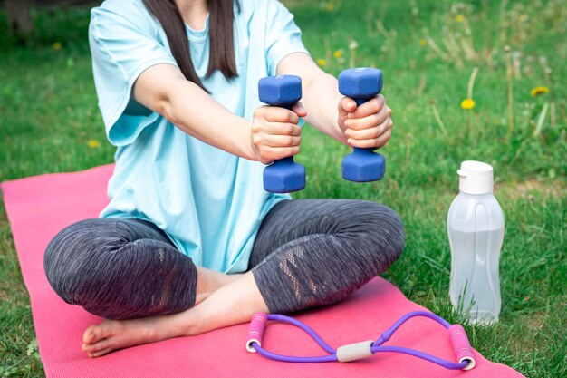 Photo gratuite femme qui s'étend avec des haltères faisant des exercices de fitness dans un parc verdoyant