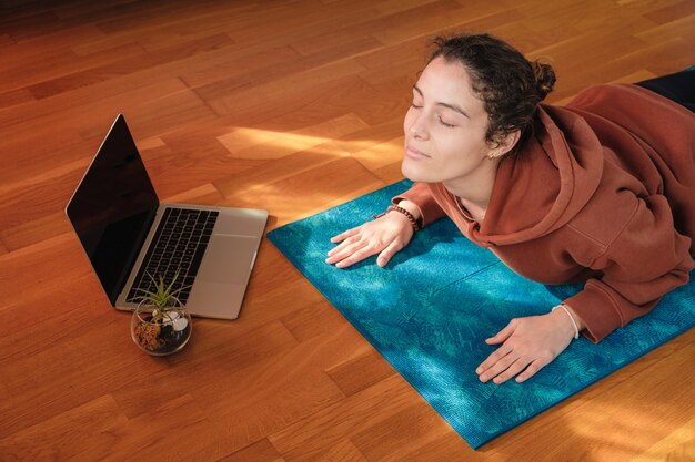 Femme qui s'étend sur un tapis pendant les cours de yoga en ligne