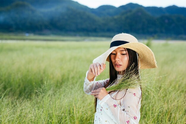Une femme qui tient une herbe dans ses mains sur un beau terrain avec une montagne.