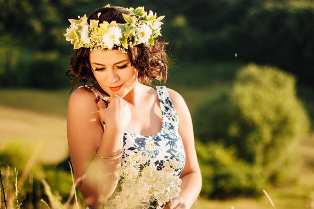 Femme de race blanche avec une couronne de fleurs ramassant des fleurs sur le terrain