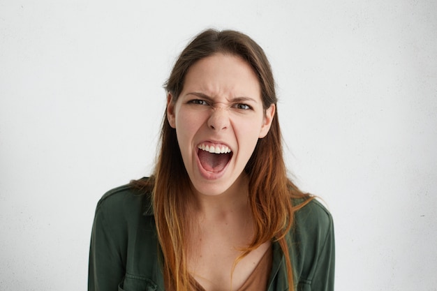 Femme de race blanche folle criant fort ouvrant sa bouche fronçant le visage avec colère démontrant ses émotions négatives.