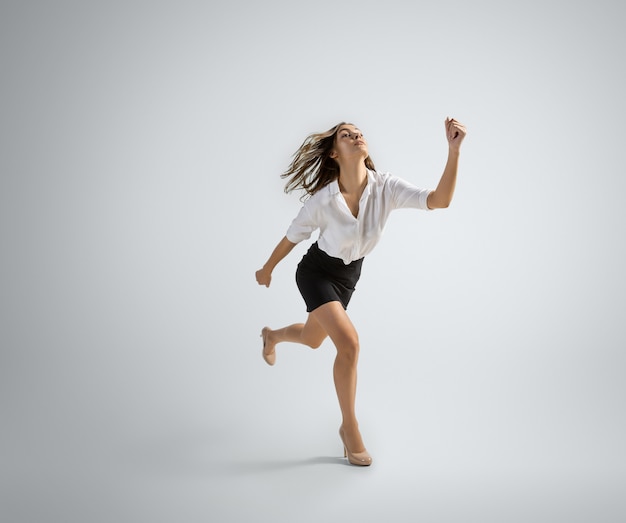 Femme de race blanche en tenue de bureau en cours d'exécution isolé sur mur gris