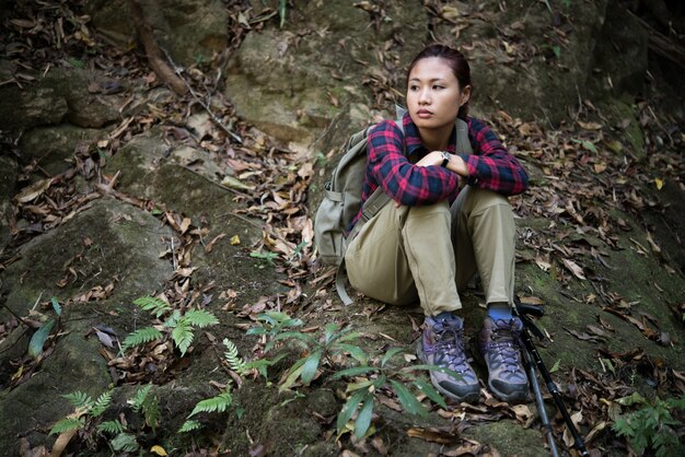 Femme randonneur en forêt prenant un repos assis à proximité cascade profiter de la nature.