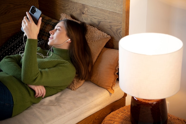 Femme recherchant quelque chose sur Internet à l'aide de son smartphone allongée sur son lit