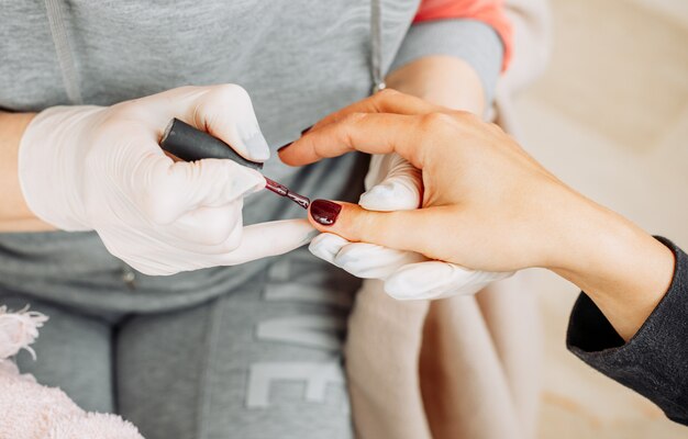 Une femme reçoit la manucure d'une femme en gants et masque dans un salon de beauté pendant la journée