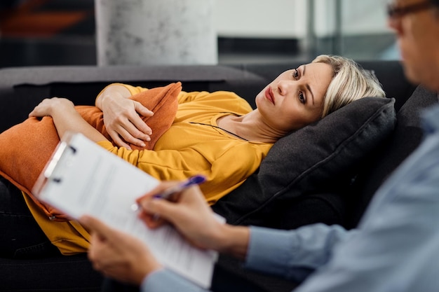 Femme réfléchie allongée sur le canapé du psychiatre lors d'un rendez-vous avec son thérapeute