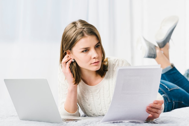 Femme réfléchie lire des documents près d&#39;un ordinateur portable