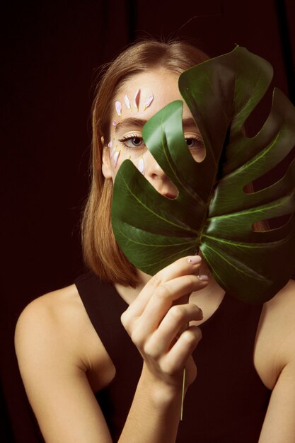 Femme réfléchie avec des pétales de fleurs sur le visage et la feuille