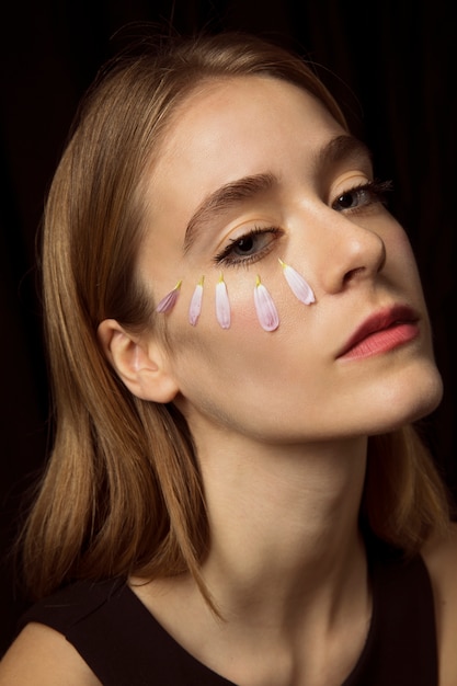 Femme réfléchie avec des pétales de fleurs sur le visage